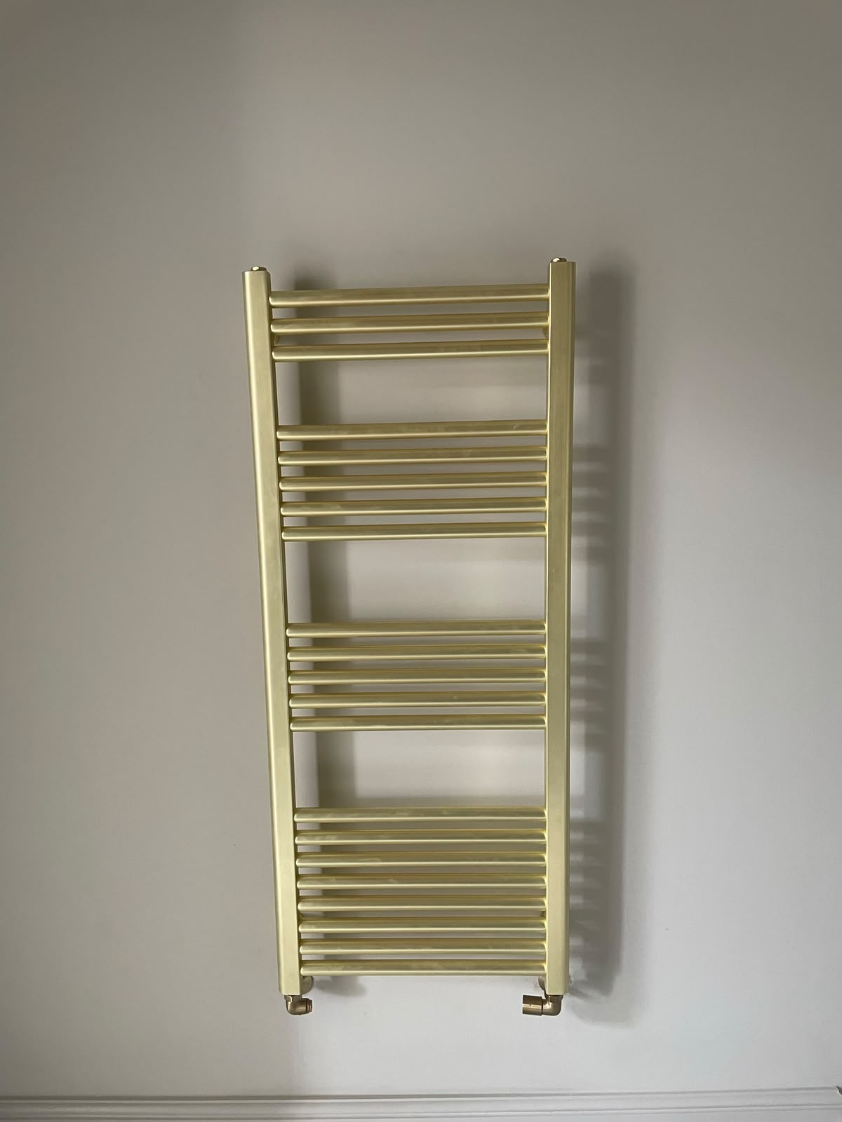 Brass towel radiator installed on a finished wall